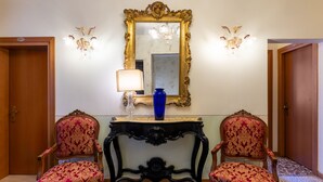 A room with two ornate chairs, a table with a vase, and a mirror with a gold frame.