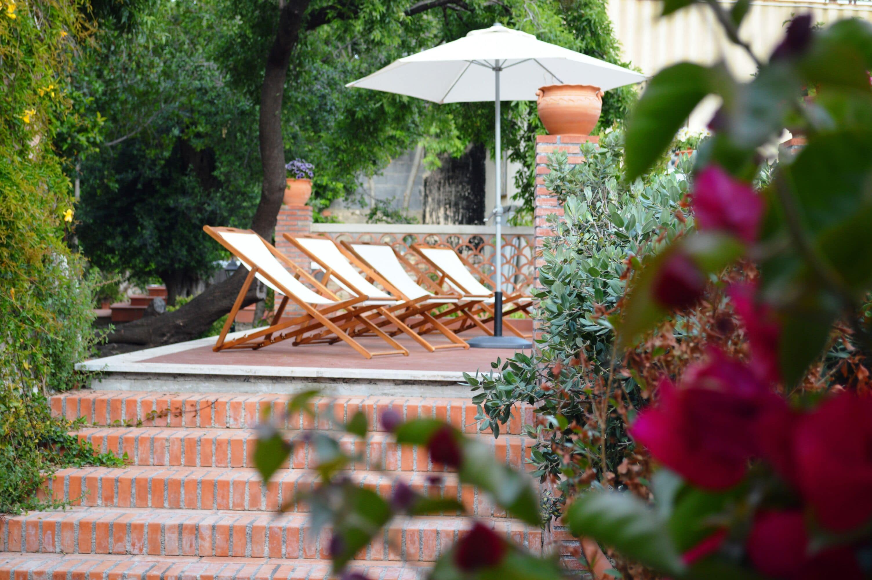 A set of outdoor lounge chairs and a white umbrella on a brick staircase surrounded by greenery.