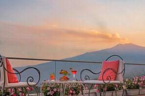 A balcony with two chairs, a table with a drink and fruit, and a view of a mountain. - Hotel Continental (Taormina)