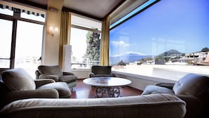 Ett hotellrum med ett stort fönster som vetter mot bergen, ett runt bord och flera soffor.