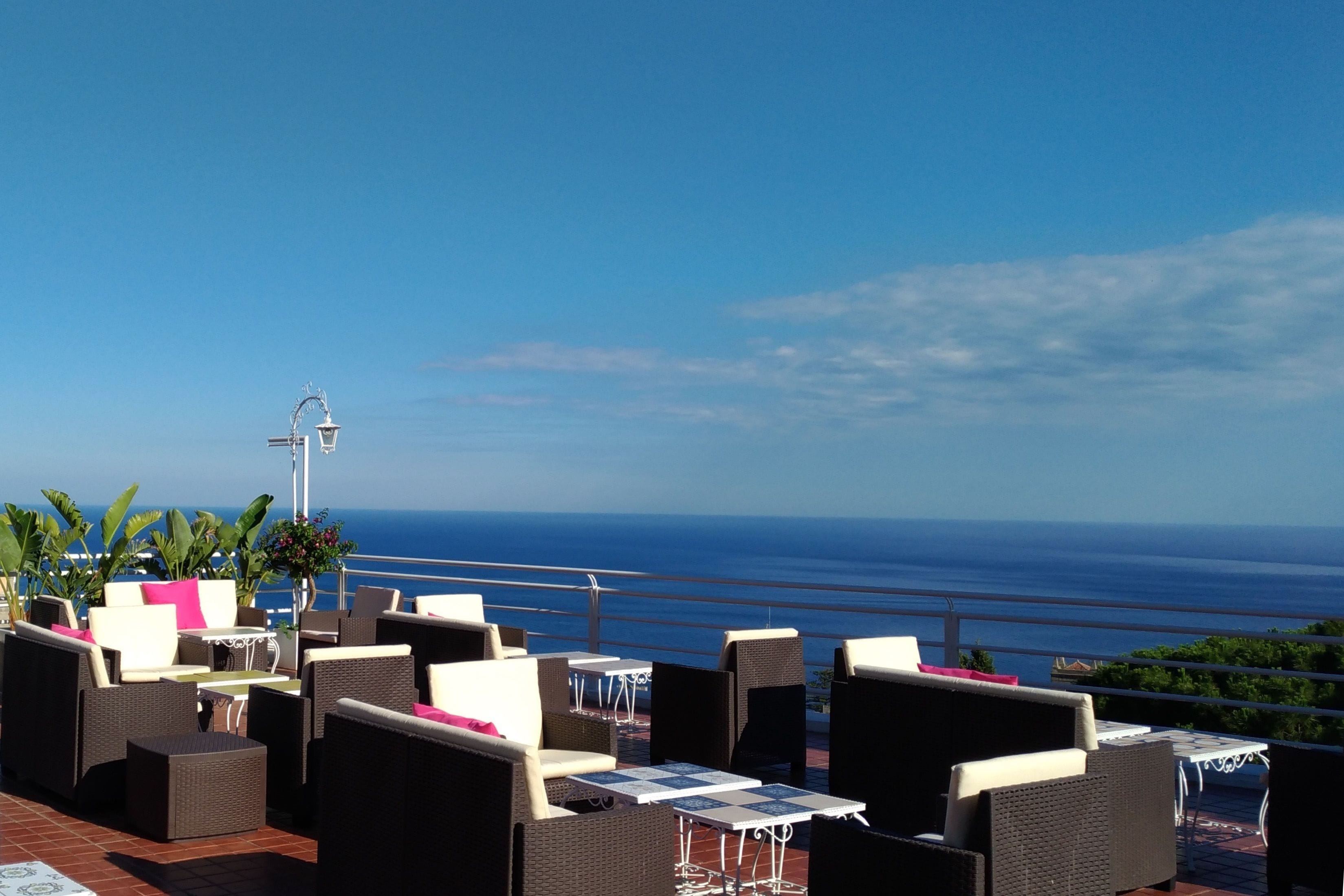 A terrace with wicker furniture and tables, overlooking a coastal view.
