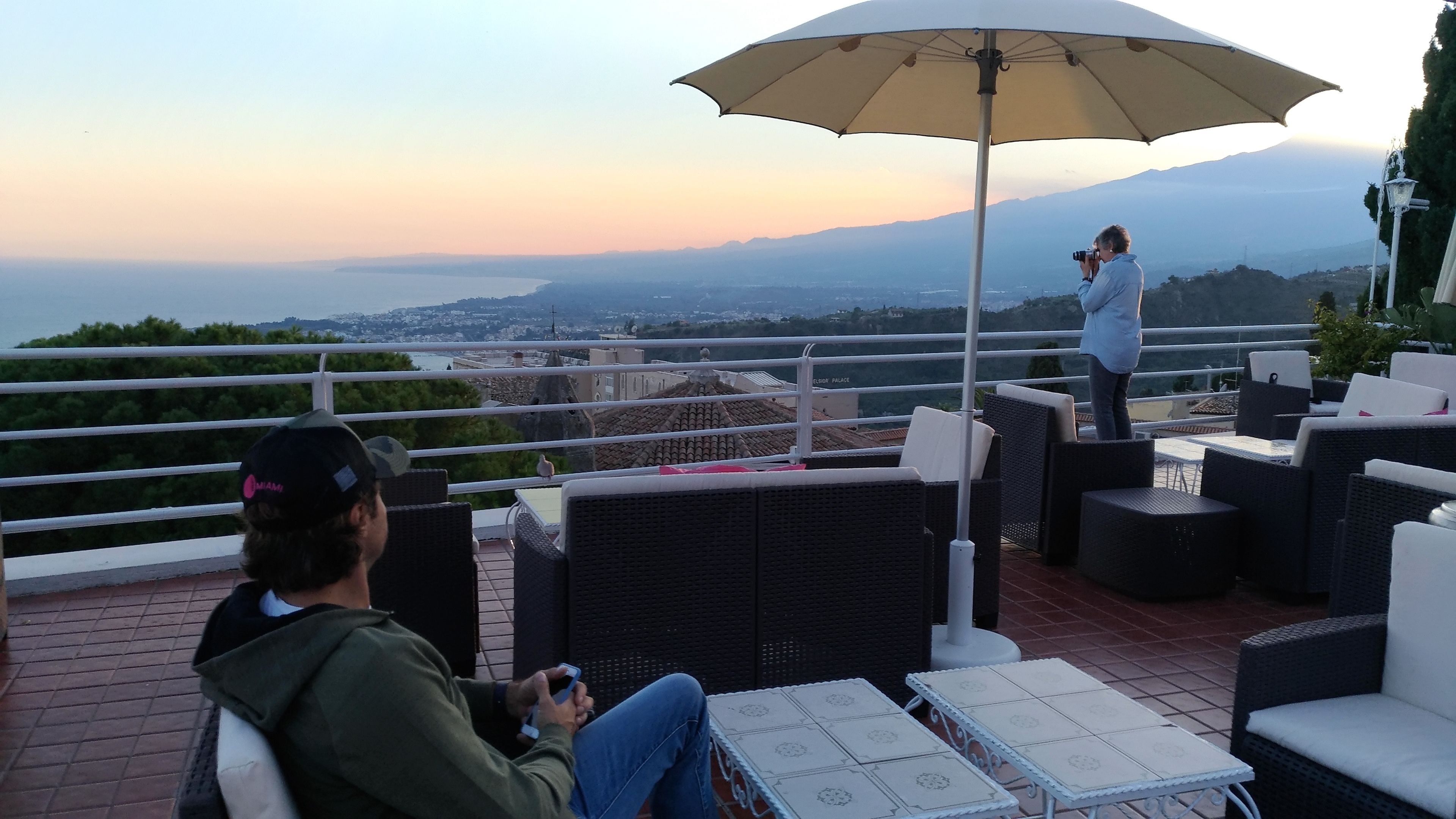 A terrace with wicker furniture, a table with a patterned tablecloth, and a view of a distant city and mountains.