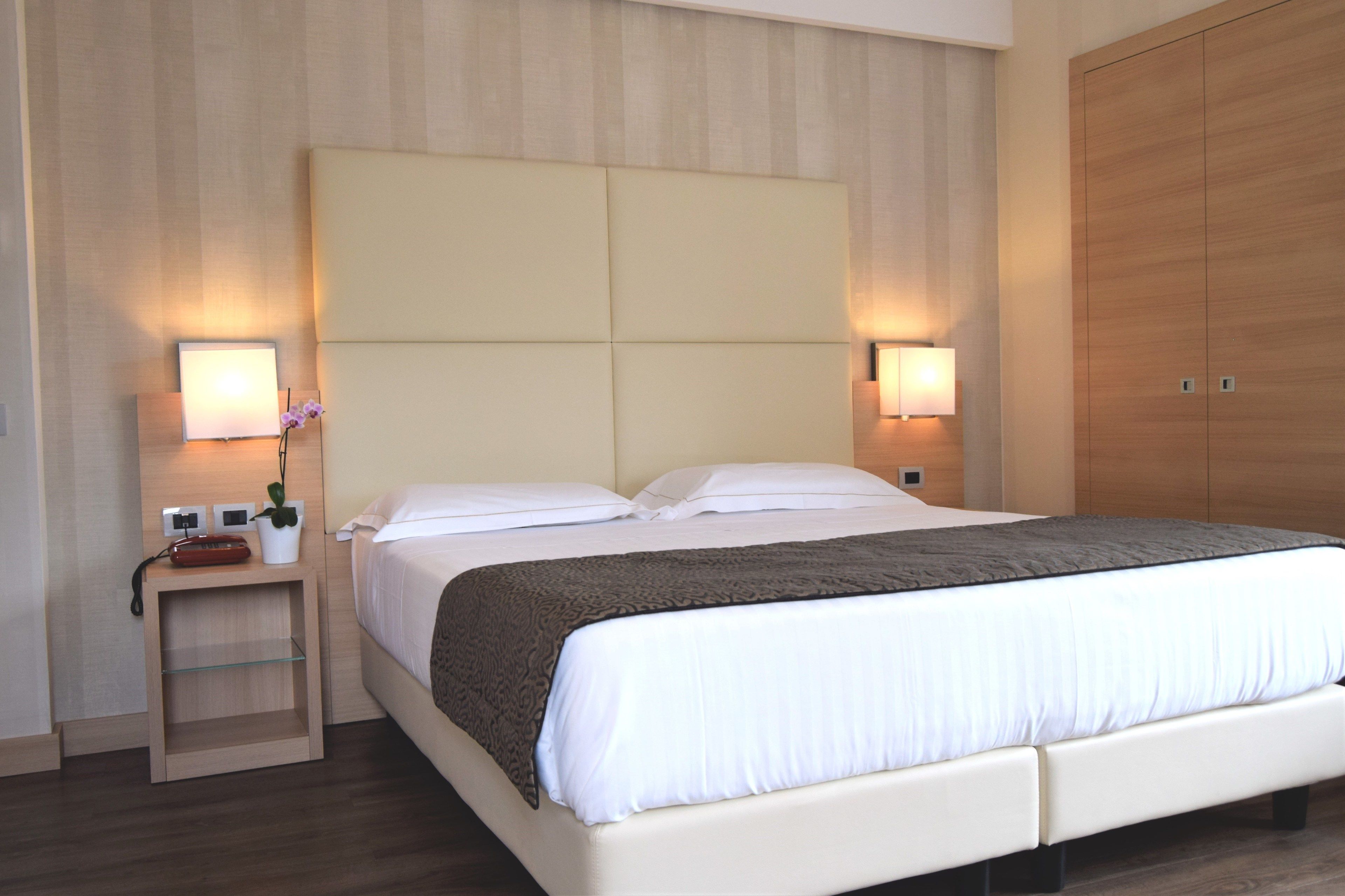 A modern hotel room with a large bed, bedside lamps, a nightstand, and a wardrobe.