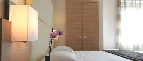 A hotel room with a bed, a nightstand, a lamp, a wardrobe, and a potted orchid.
