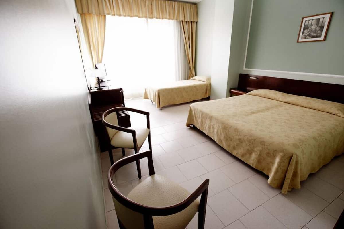 Una habitación de hotel con una cama, un escritorio con silla, una mesita de noche y una ventana con cortinas.