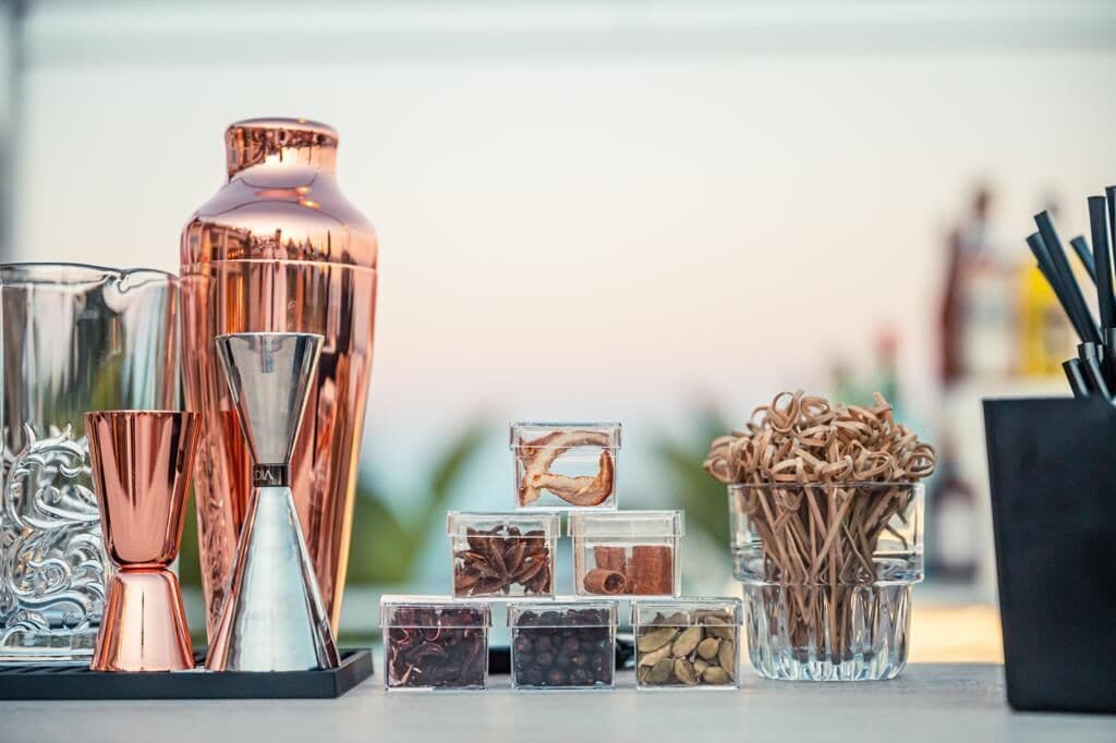 A variety of glassware and containers, including a tall copper-colored bottle, several glass tumblers, and small clear containers holding spices and herbs.