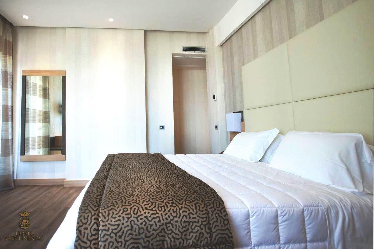 A modern hotel room with a large bed, a mirror, a wardrobe, and a window with curtains.