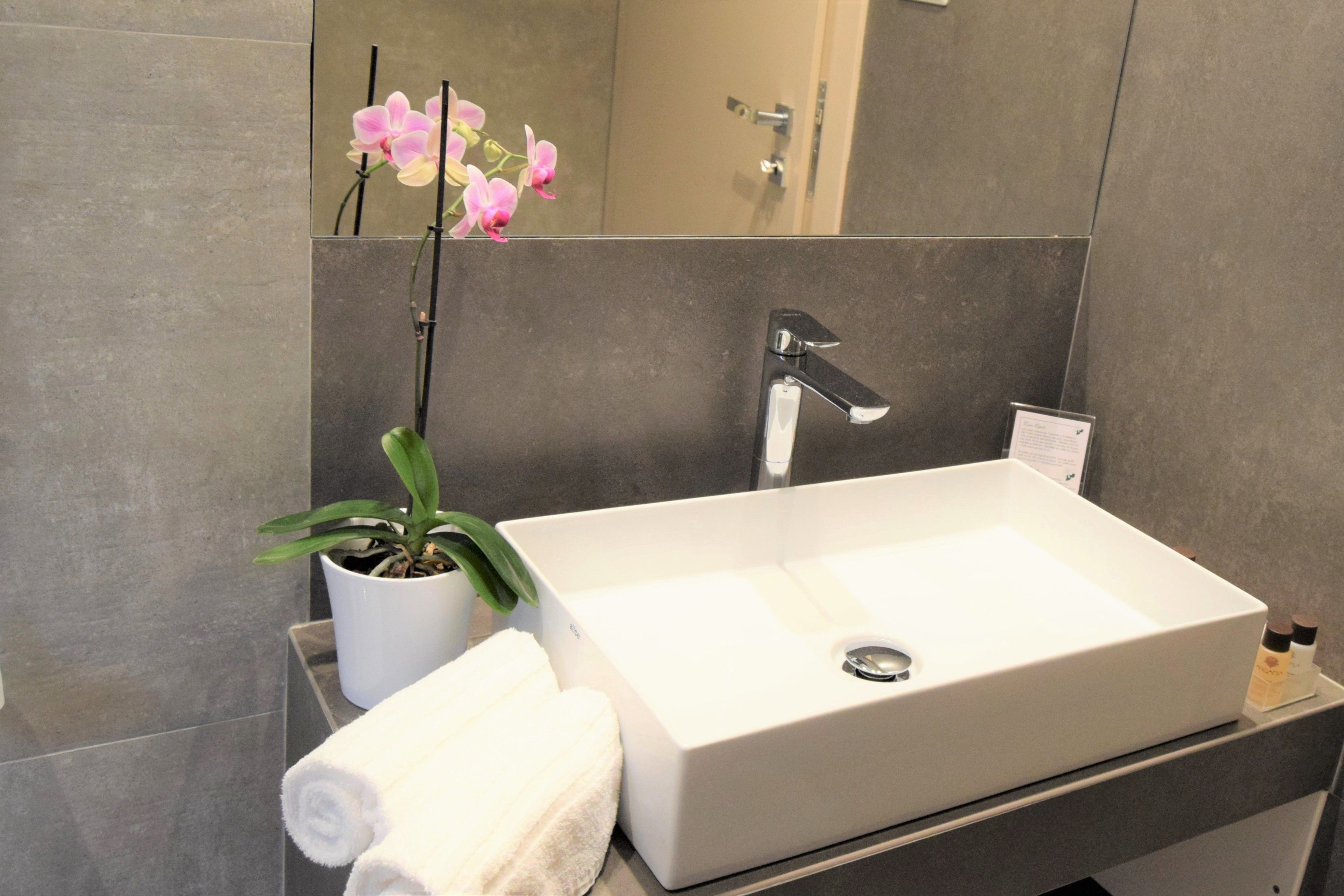 Un baño moderno con un lavamanos blanco, una orquídea en maceta y una toalla.