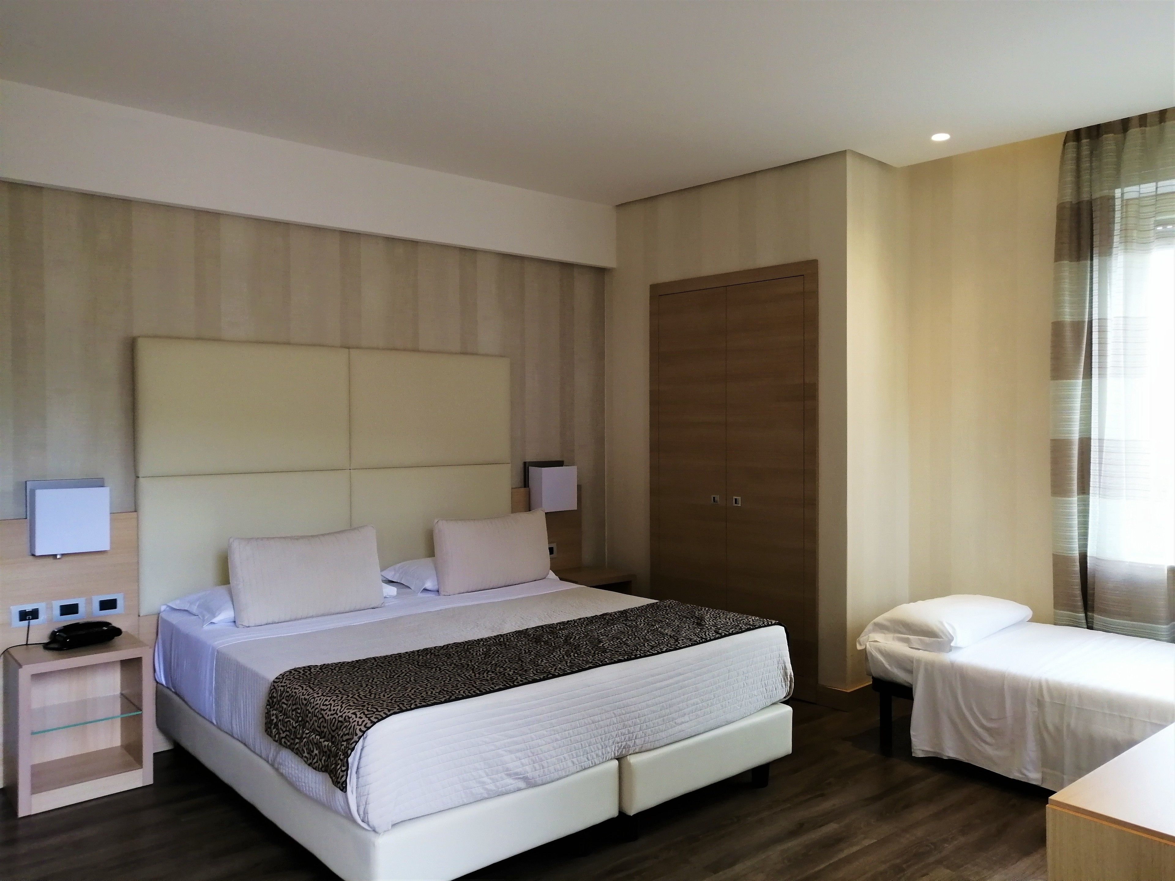 A hotel room with a large bed, bedside tables, a wardrobe, and a small desk.