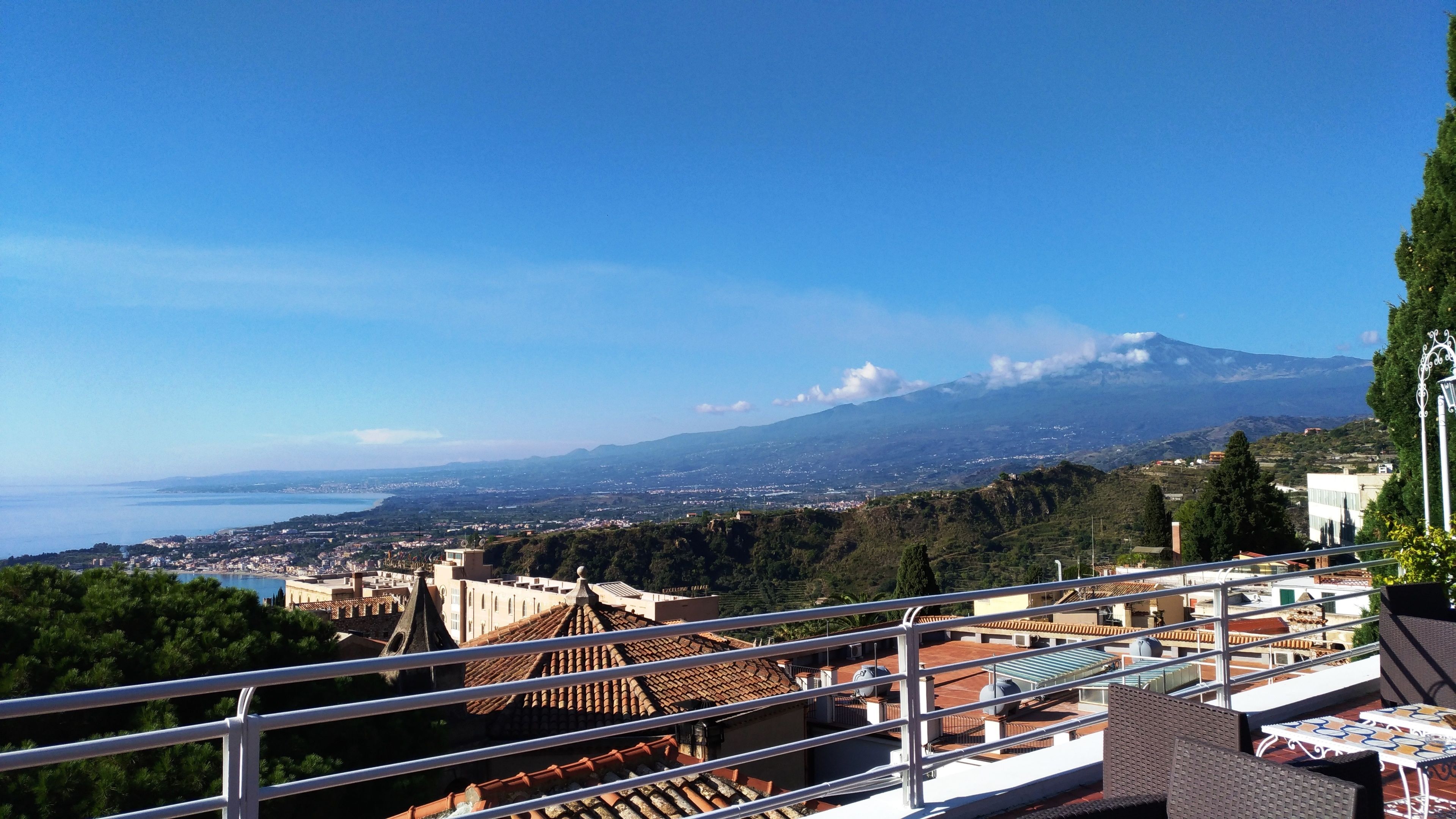 A terrace with a view of a coastal town, a mountain in the background, and a clear sky.