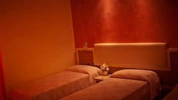 A small, dimly lit room with two beds, a red curtain, and a white headboard.