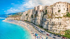 A coastal town with a beach lined with colorful umbrellas, a road running parallel to the beach, and buildings built into the cliffside.