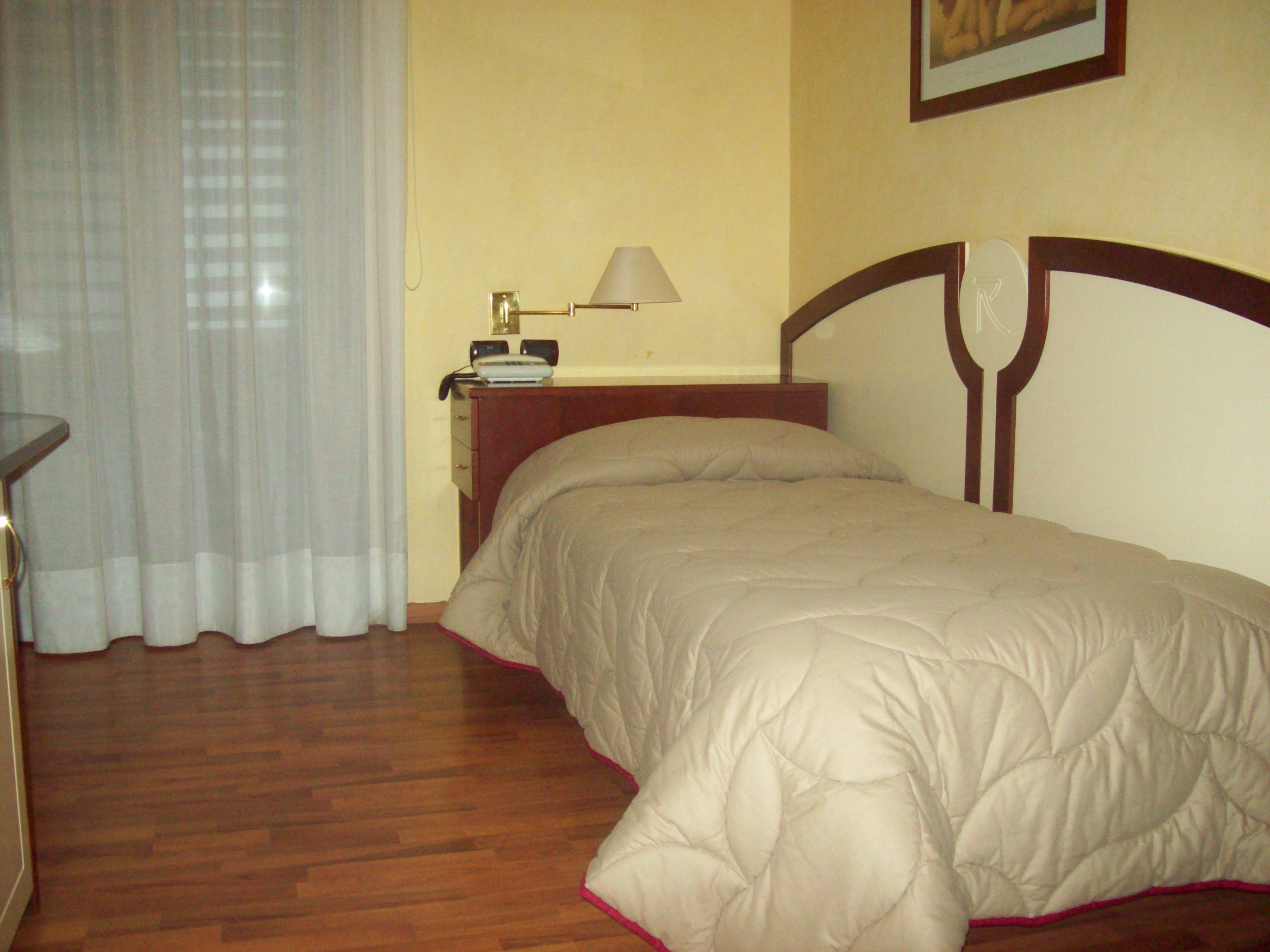 Camera da letto con un letto, un comodino, una lampada e una finestra con tende.