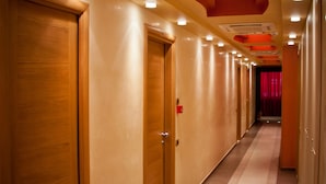 A hotel corridor with wooden doors, a patterned carpet, and recessed lighting.