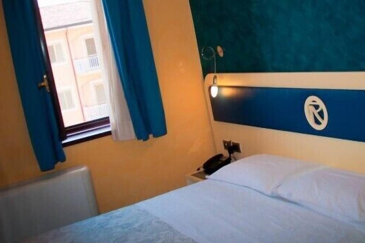 Habitación de hotel con una cama, una mesita de noche, un teléfono y una ventana con cortinas.
