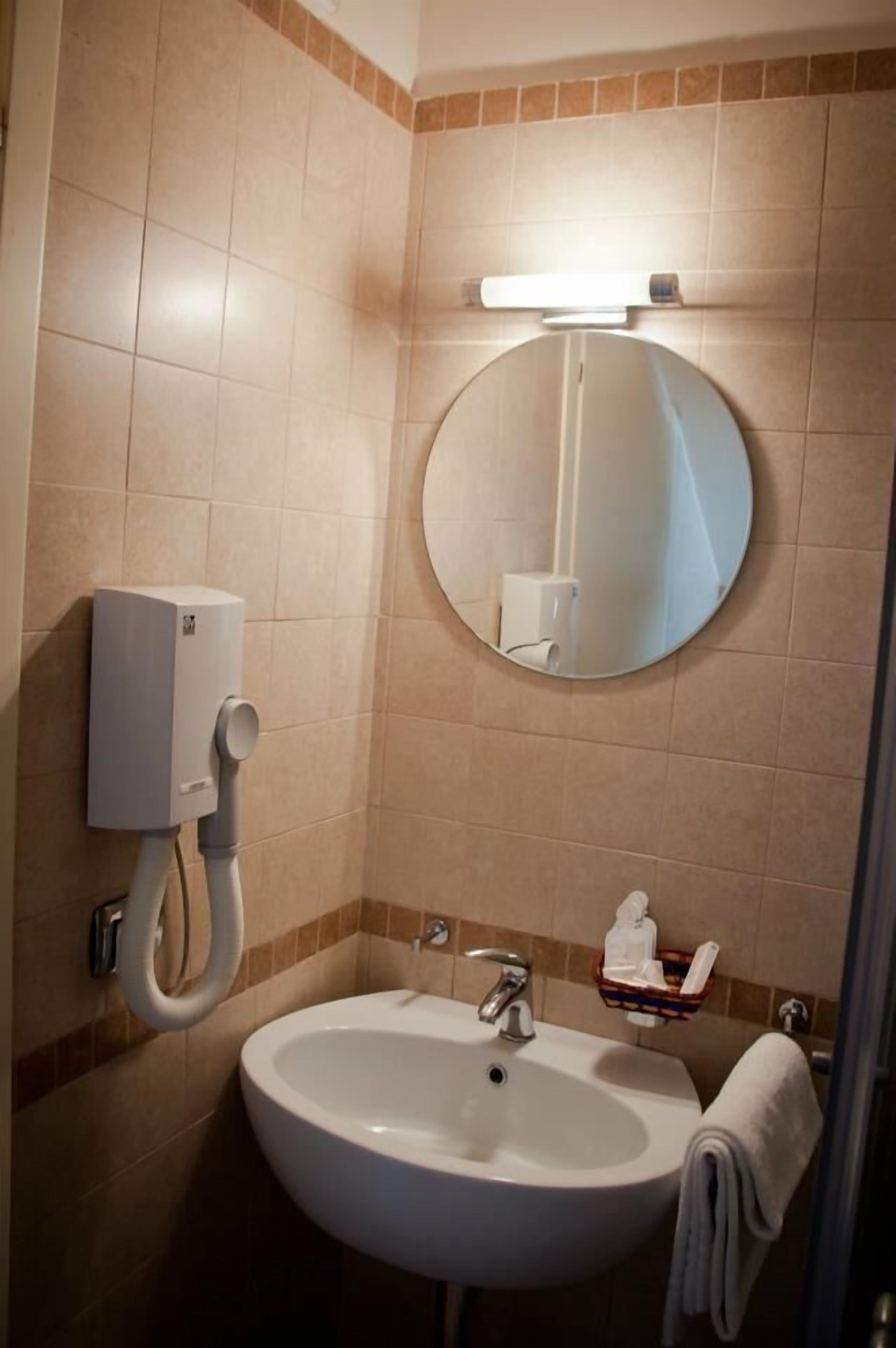 Un bagno con lavandino, specchio, portasciugamani e dispenser per sapone.