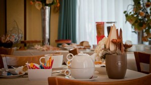 A dining table set with a white teapot, cups, and a brown mug, surrounded by floral arrangements and a vase.