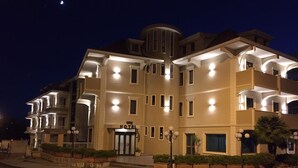 A multi-story hotel with a central entrance, balconies, and a well-lit facade.