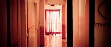 A narrow hallway with wooden doors on the left and a red curtain at the end.