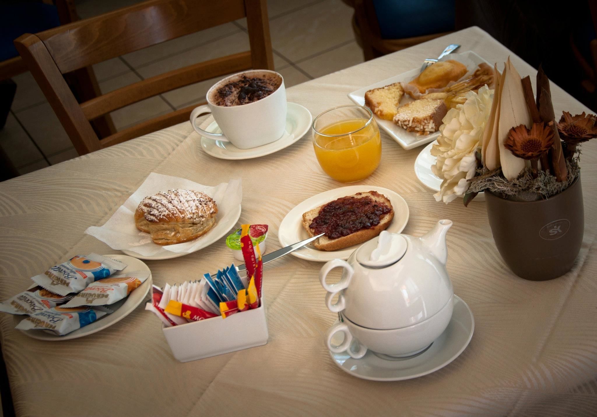 A breakfast table with a cup of coffee, orange juice, pastries, and a teapot.
