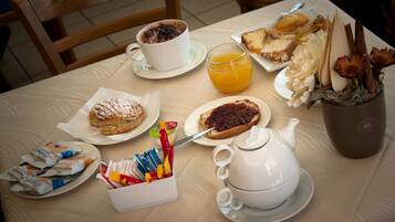 A breakfast table with a cup of coffee, orange juice, pastries, and a teapot.