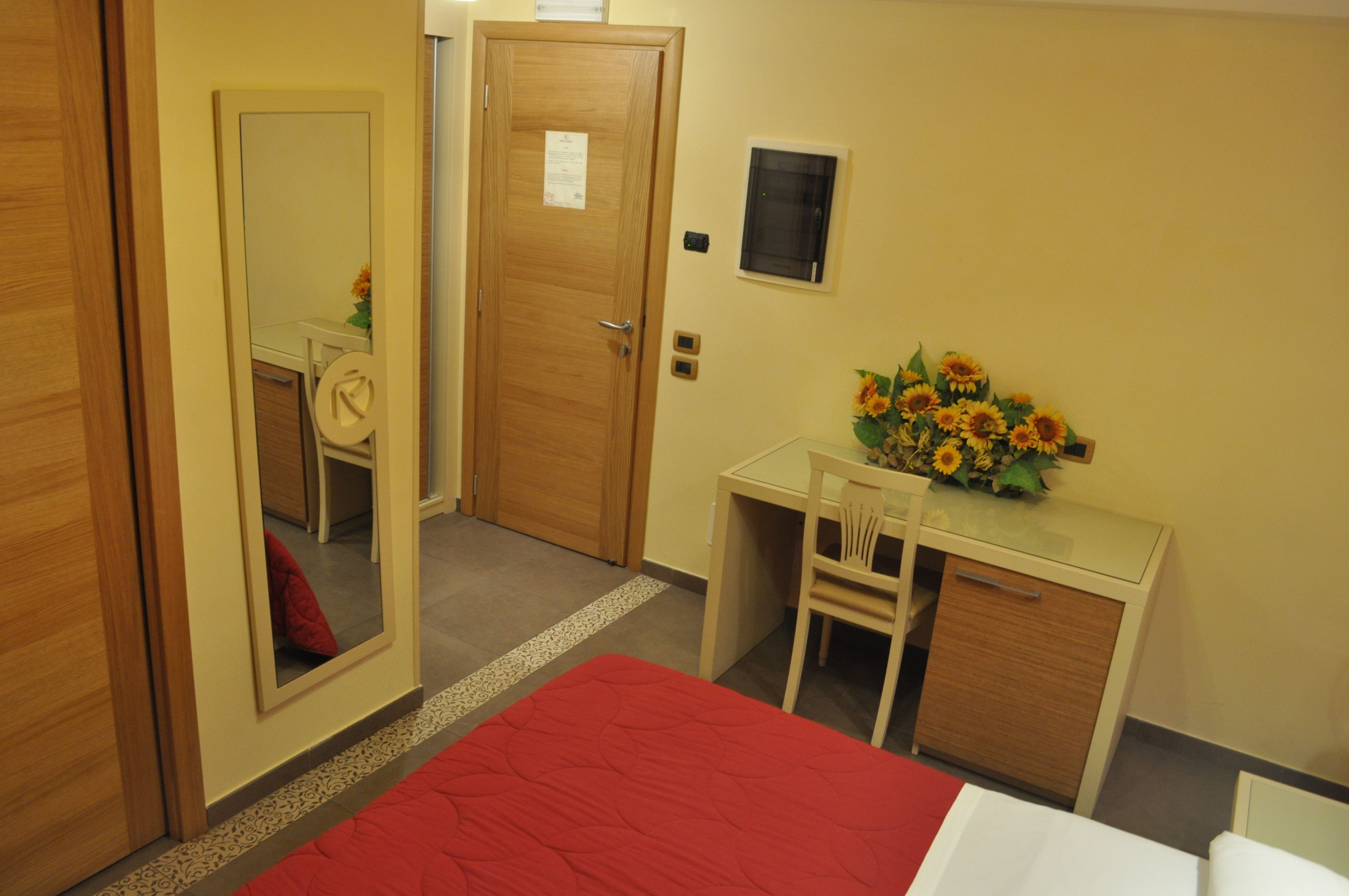 A hotel room with a bed, a desk, a chair, a mirror, and a wall-mounted TV.