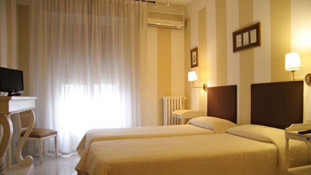 Una habitación de hotel con dos camas, un escritorio con una silla, televisión y una ventana con cortinas.