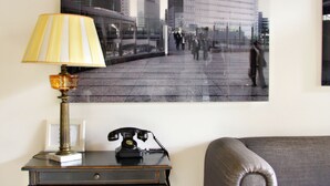 Una habitación con una mesa, una lámpara, un teléfono, un sofá y una fotografía de gran tamaño con una vista panorámica de la ciudad.