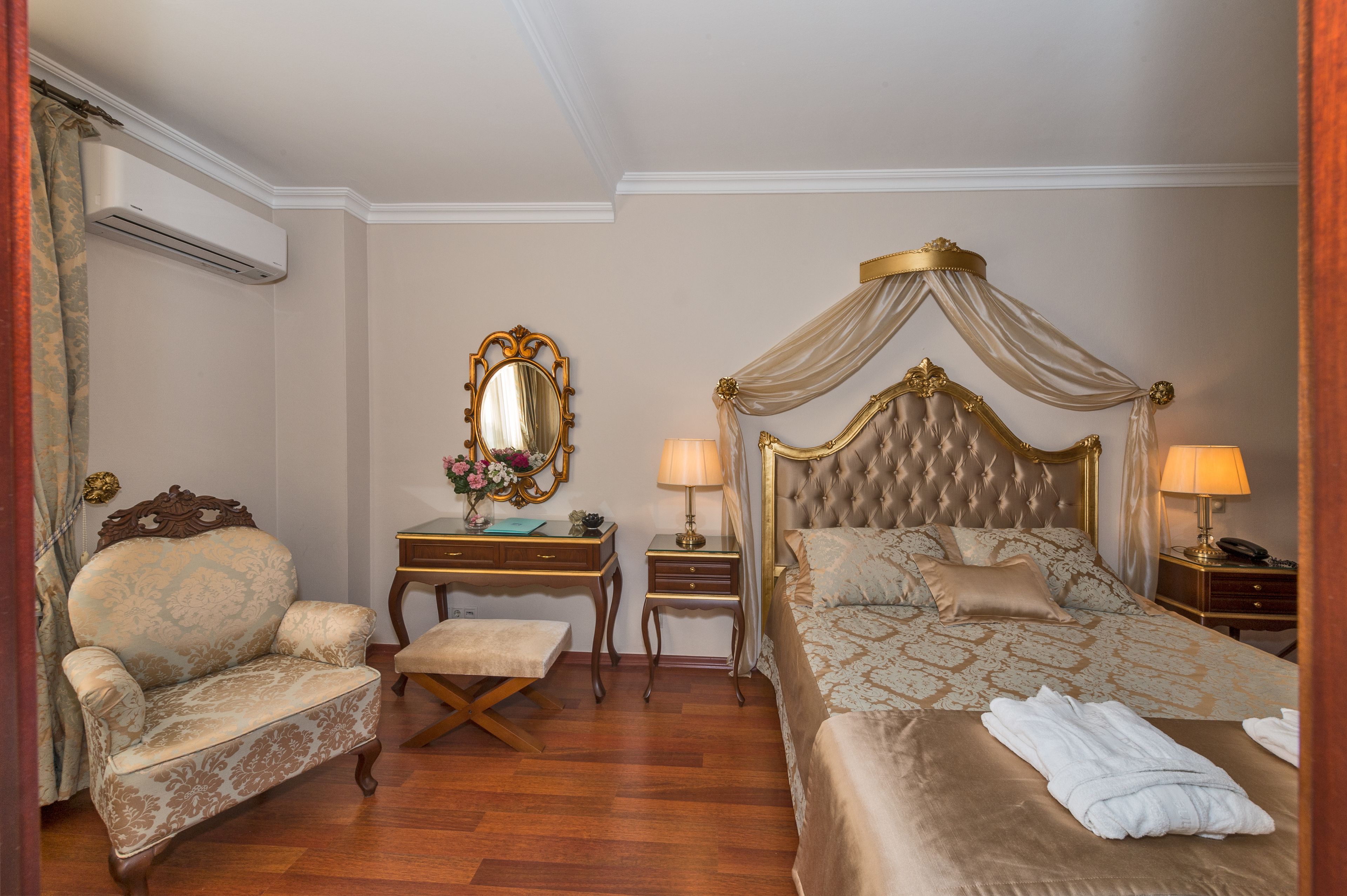 A bedroom with a four-poster bed, a vanity with a mirror, a chair, and a desk.