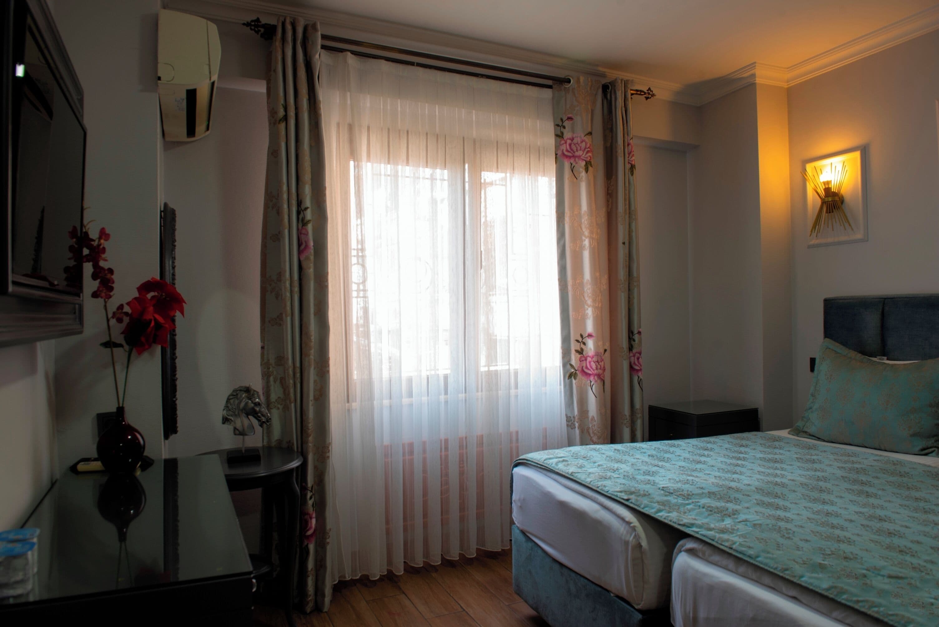 A hotel room with a bed, a bedside table, a mirror, and a window with curtains.