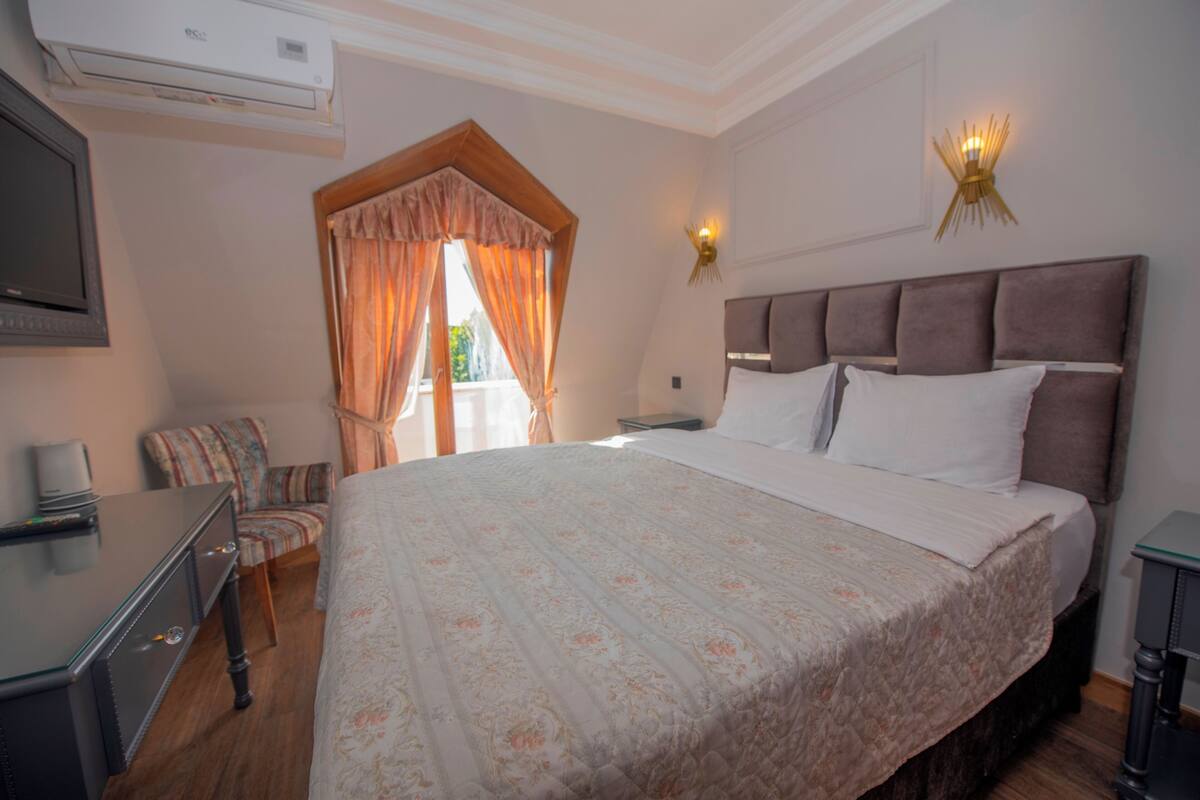 A hotel room with a large bed, a desk, a chair, a TV, and a window with curtains.
