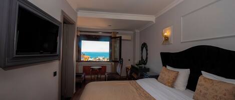 Un cuarto de hotel con cama, televisor, escritorio y silla, y vista al mar.