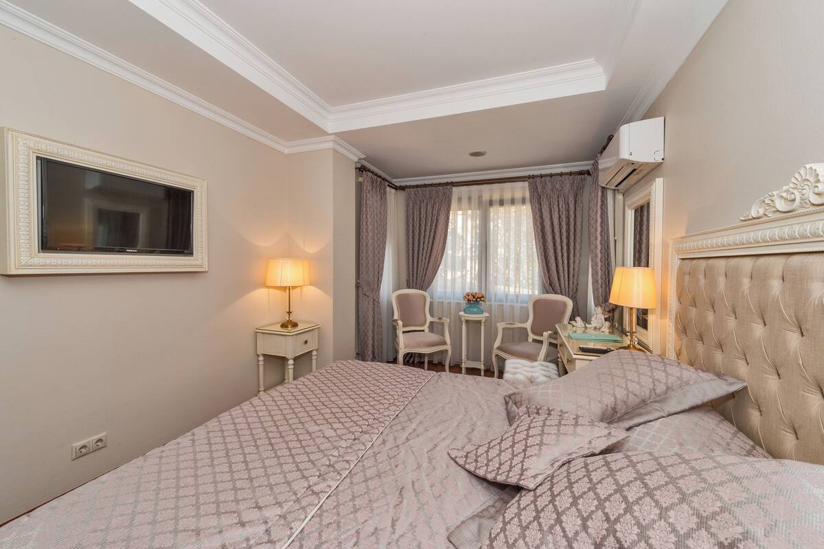 A hotel room with a large bed, two bedside tables, a desk, a chair, and a television.
