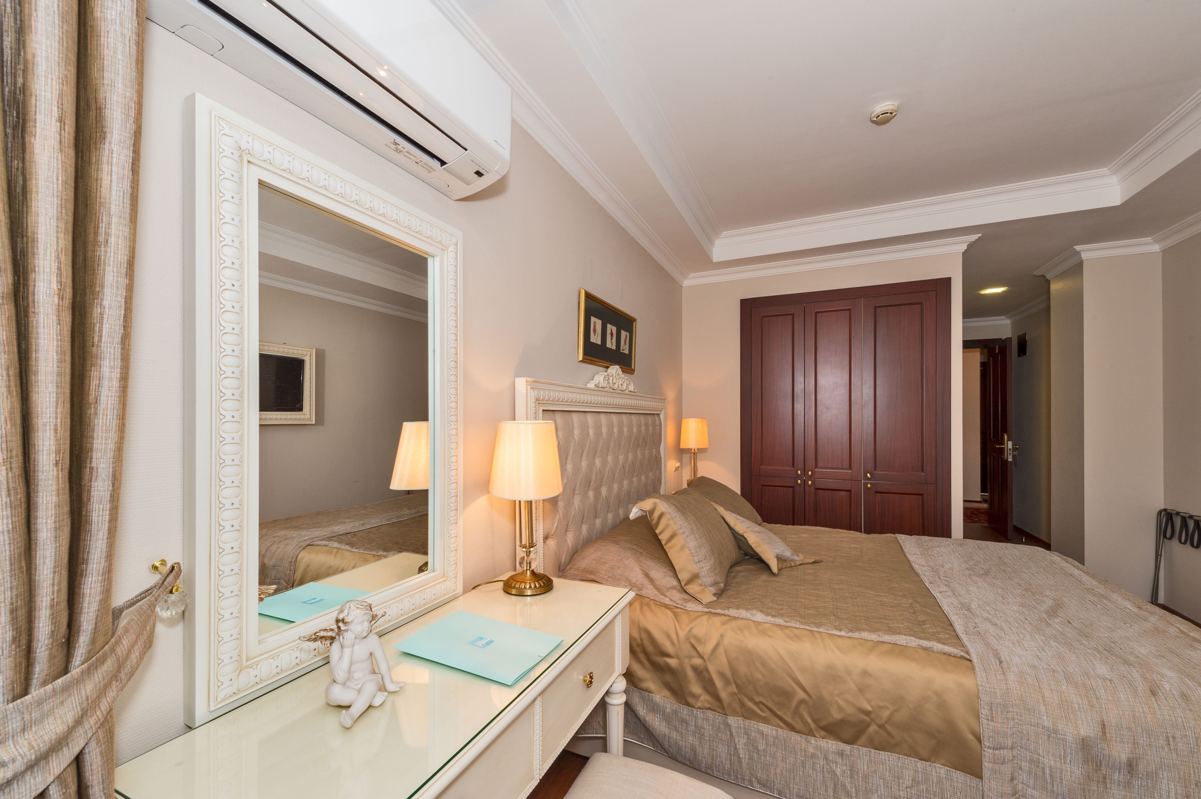 A hotel room with a large mirror, a bed with a headboard, a dresser, and a door leading to another room.