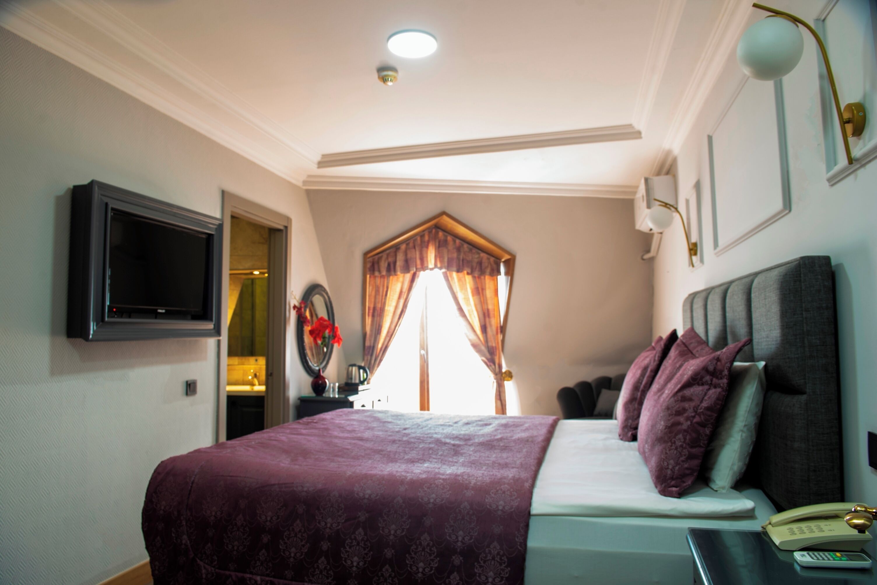 Ein Schlafzimmer mit Bett, Nachttisch, Lampe und einem an der Wand befestigten Fernseher.