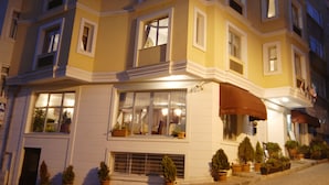 A multi-story hotel with a yellow facade, multiple windows, and a ground-level entrance with potted plants. - Hotel Daphne - Special Class (Istanbul)