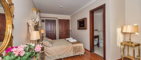 A bedroom with a bed, bedside lamps, a mirror, a vase with flowers, and a wooden floor.