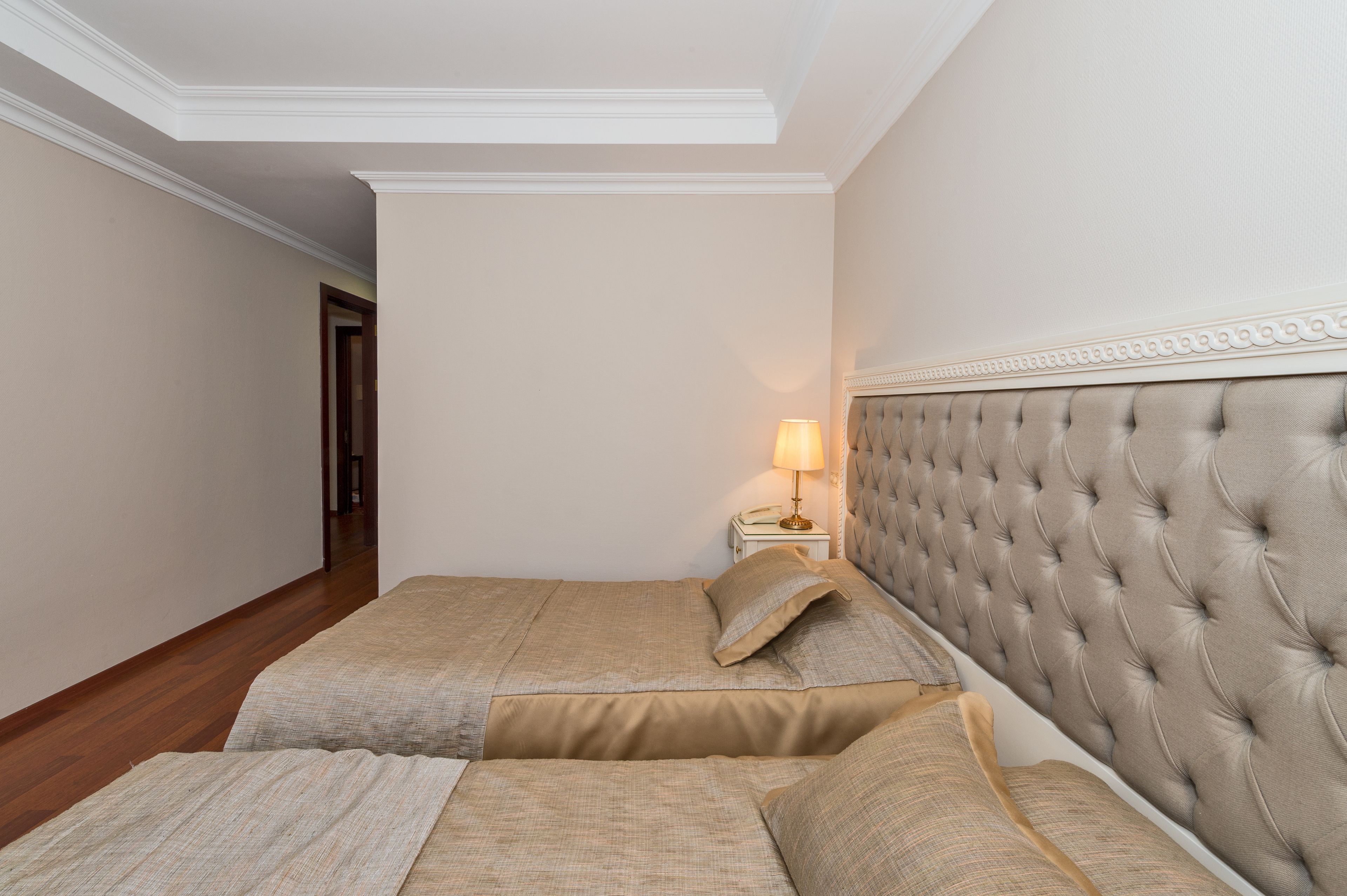 Une chambre avec deux lits, une table de chevet avec une lampe et une porte donnant sur une autre pièce.