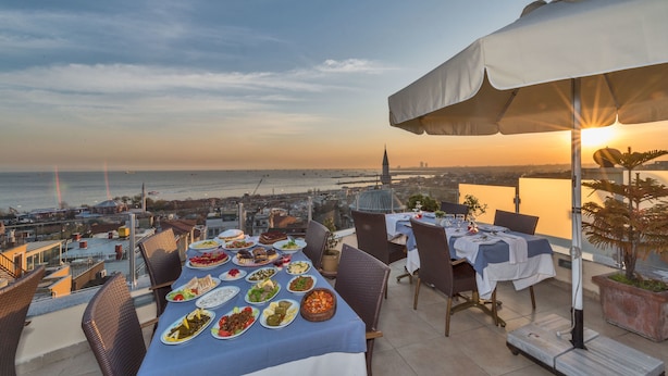 A rooftop dining area with a table set for a meal, overlooking a cityscape and the sea. - Hotel Daphne - Special Class (Istanbul)