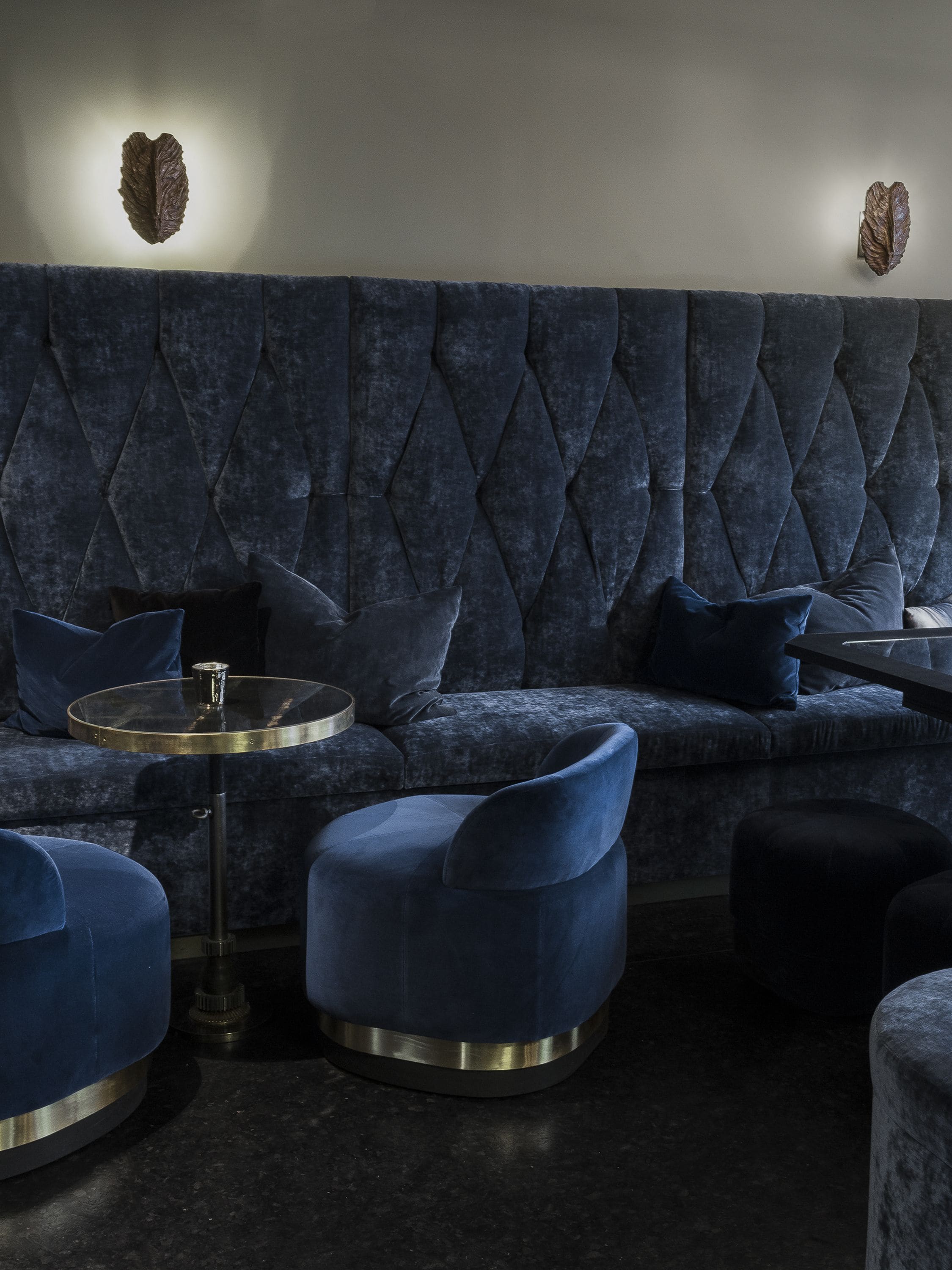 A dark blue upholstered sofa with a tufted backrest, a round glass table with a metal base, and matching blue armchairs.