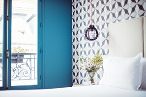 A bedroom with a large window, a geometric patterned wall, a hanging lantern, and a vase with flowers. - Monsieur Cadet Hôtel & Spa (Paris)
