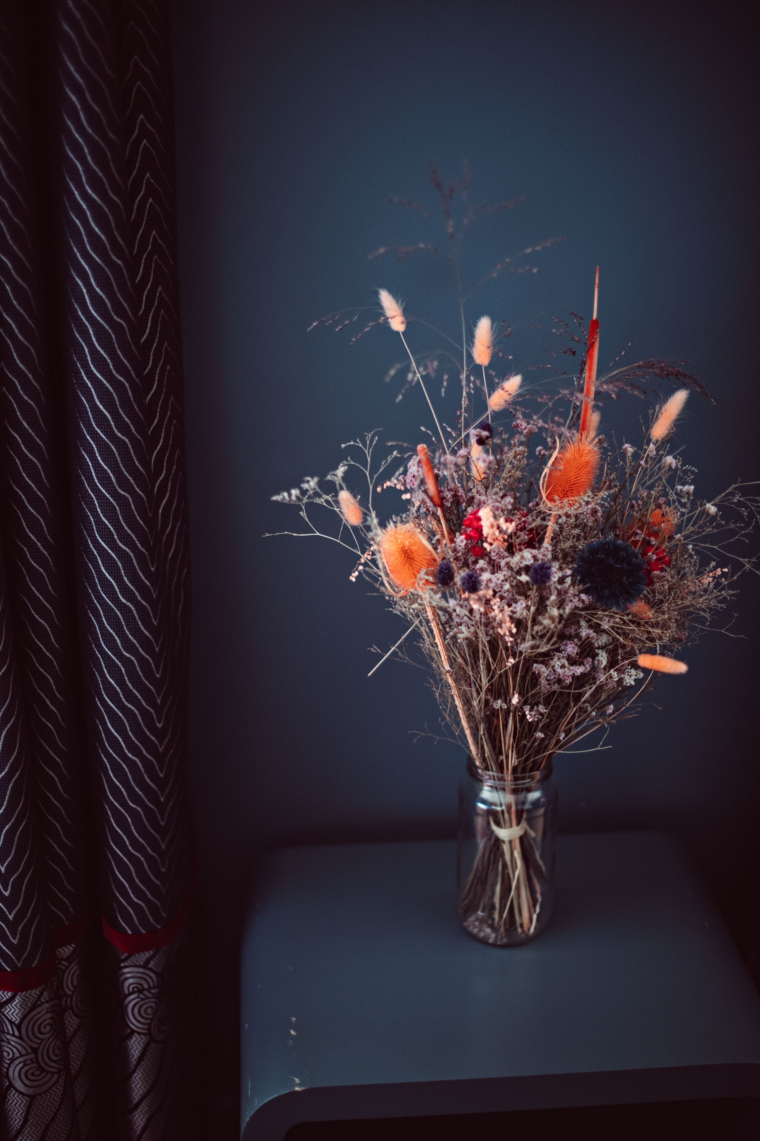 A vase of dried flowers on a dark surface.