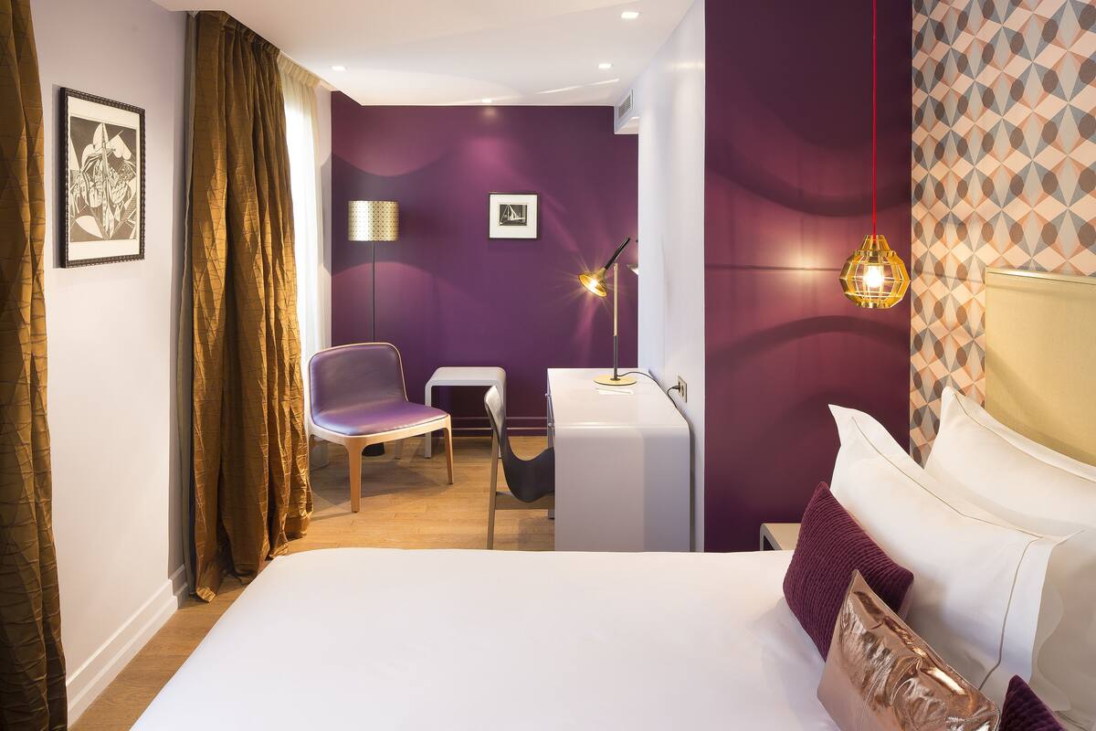 A modern hotel room with a large bed, a desk, and a chair.