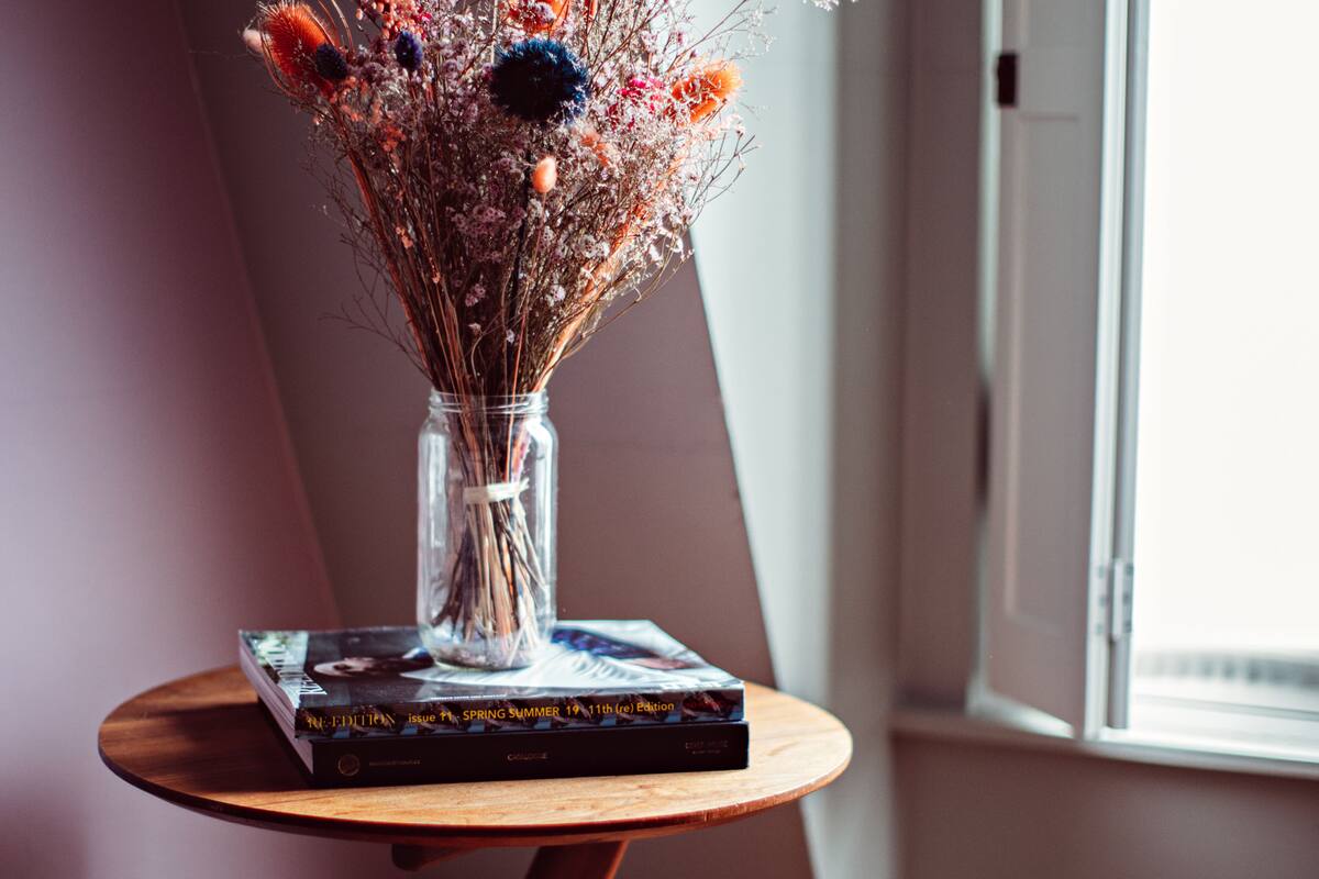 A vase with dried flowers on a wooden table next to a book.