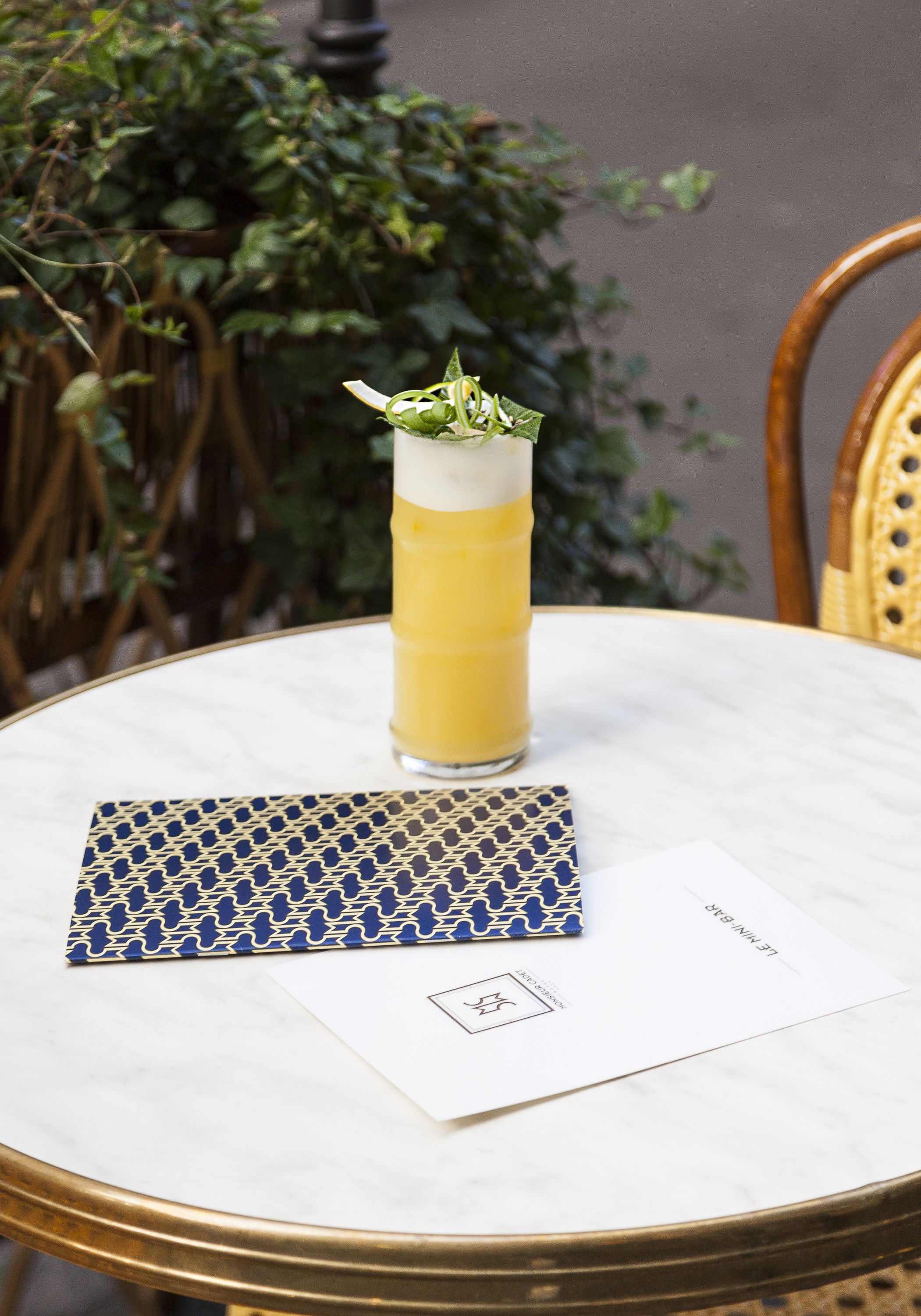 A tall glass of layered drink on a marble table with a patterned napkin and a menu.