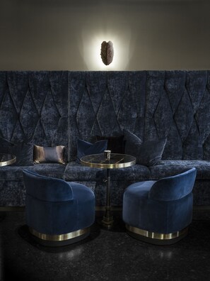 Een donkerblauwe gestoffeerde bank met een gebonden rugleuning, een ronde glazen tafel met een metalen voet en twee bijpassende fauteuils.