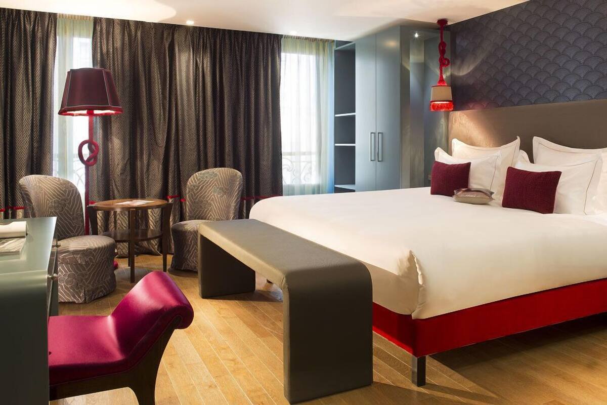 A modern hotel room with a large bed, a desk, a chair, and a bench.