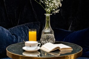 A round table with a white cup, saucer, a glass of orange juice, a clear glass vase with white flowers, and an open book. - Monsieur Cadet Hôtel & Spa (Paris)