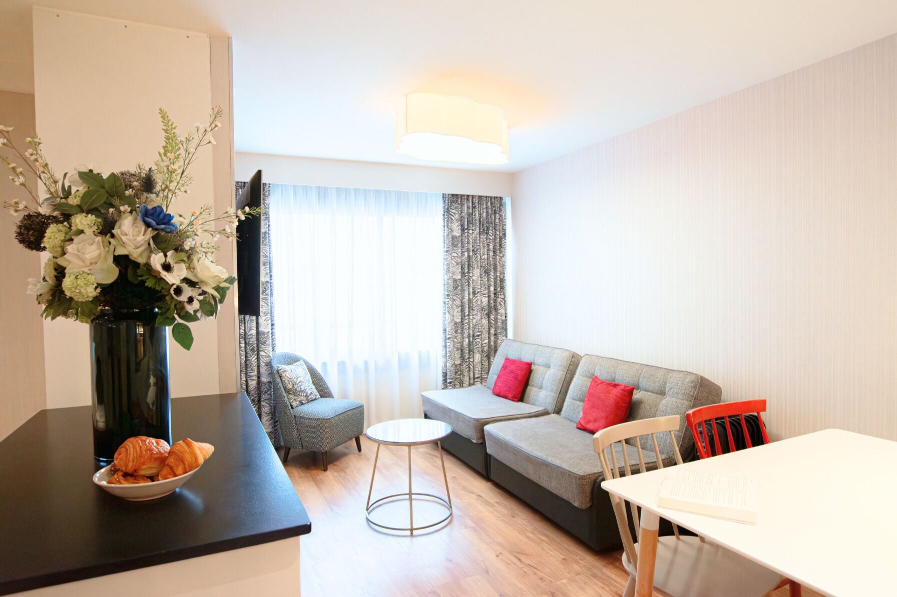 A modern living room with a sofa, chairs, a small round table, and a vase of flowers on a counter.