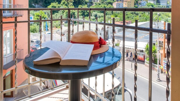 Un balcón con una mesa, un libro y un sombrero de paja.